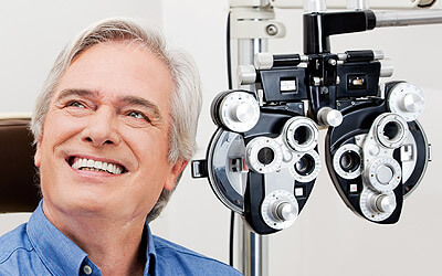 Man smiling while sitting next to eye exam equipment