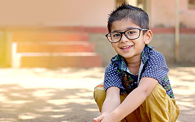 Boy sitting on the ground with glasses on smiling